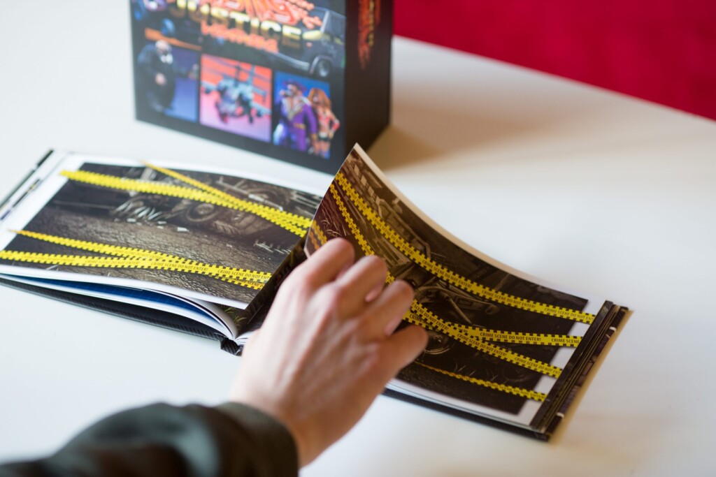 Hand holding open a hardcover book with yellow and black striped cover design, with additional copies and a product box
