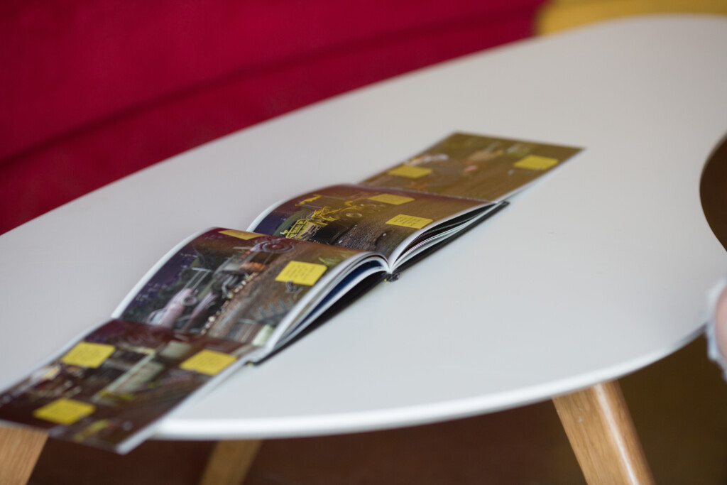 Open catalogue with glossy laminated cover featuring yellow and dark imagery, fanned pages visible on white surface with
