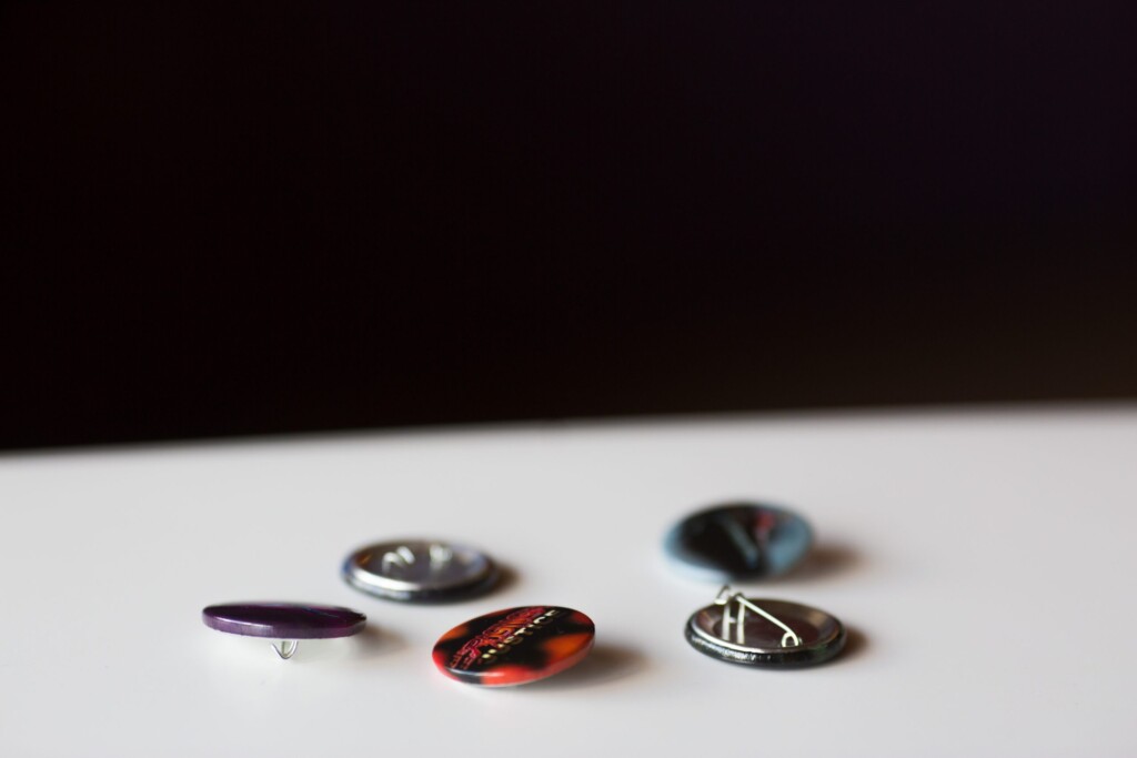 Five decorative buttons with various finishes including metallic, tortoiseshell, and embossed surfaces on a white surface.