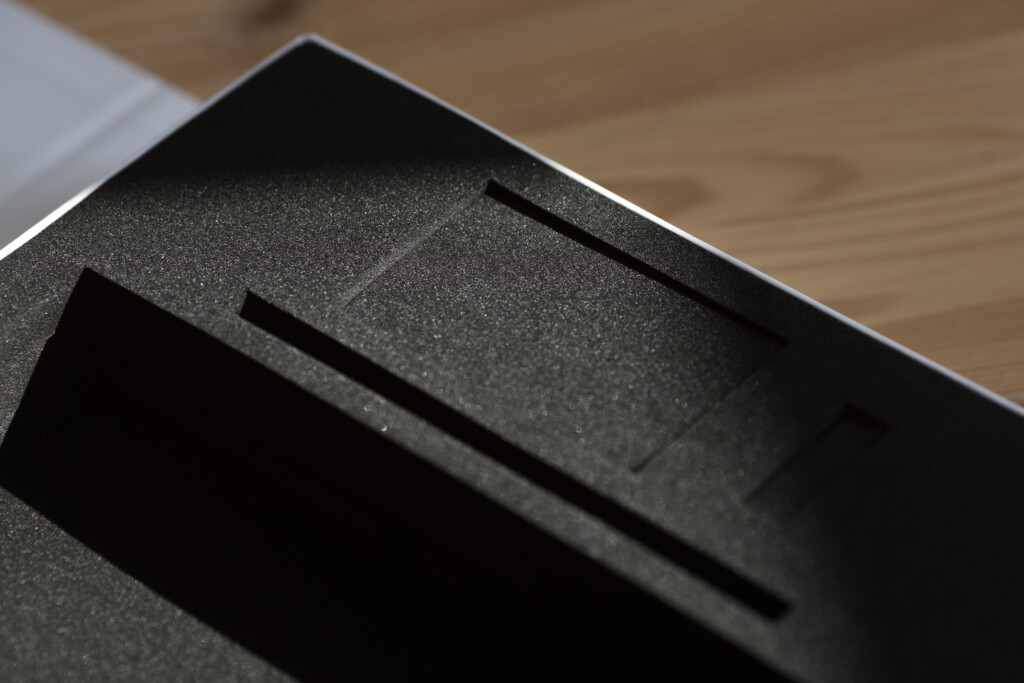 Close-up of a black rigid box interior with grey foam insert and recessed compartments on wooden surface.