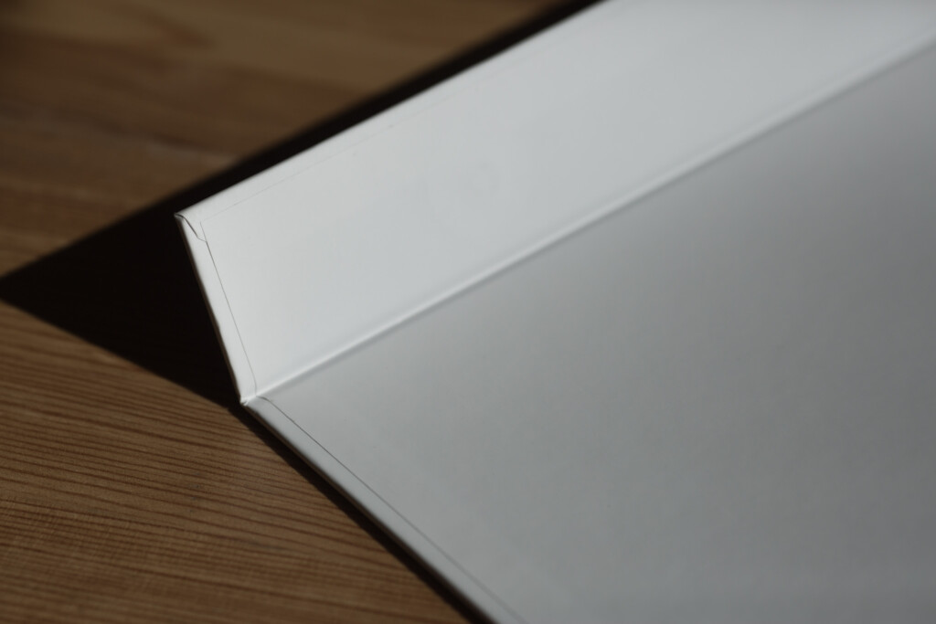 Open hardcover book with white endpapers and grey pages on wooden surface.