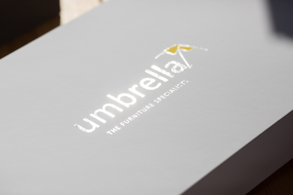Umbrellat branded box with white cover and gold foil-stamped logo and tagline "The Furniture Specialist