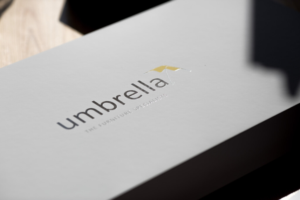 White business card or packaging box with yellow umbrella icon and Umbrella wordmark printed on surface.