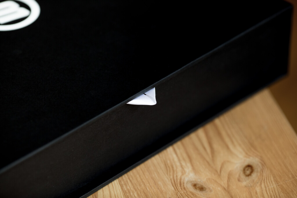 Black rigid box with white foil-stamped detail on edge, positioned on wooden surface.