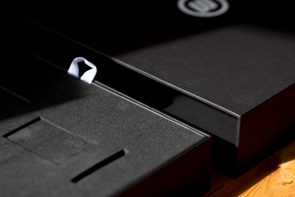 Black rigid boxes with red sides stacked together, showing embossed detail on the top box.