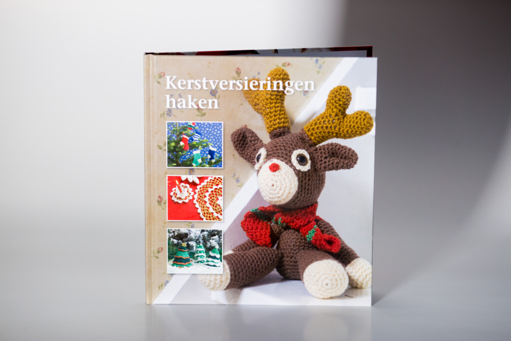 Dutch crochet craft book "Kerstversieringen haken" with crocheted reindeer toy wearing red scarf displayed on cover.