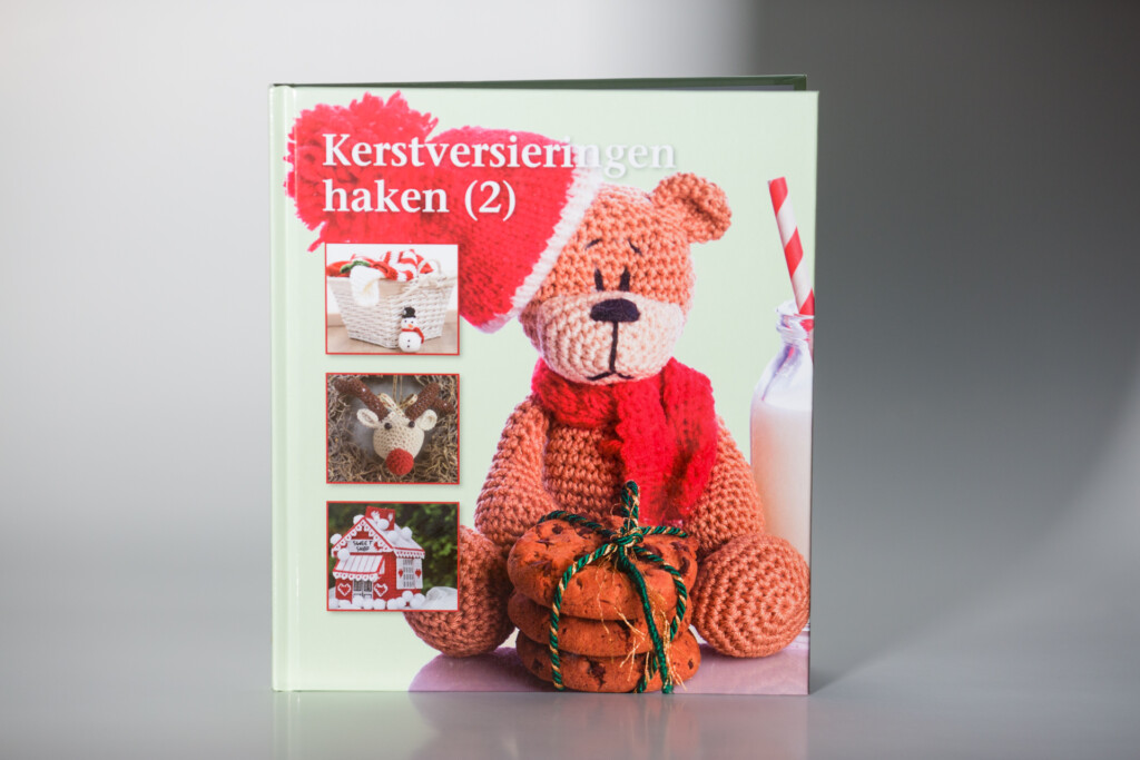 Softcover craft book titled Kerstverstieringen haken (2) featuring a crocheted teddy bear with red scarf holding a