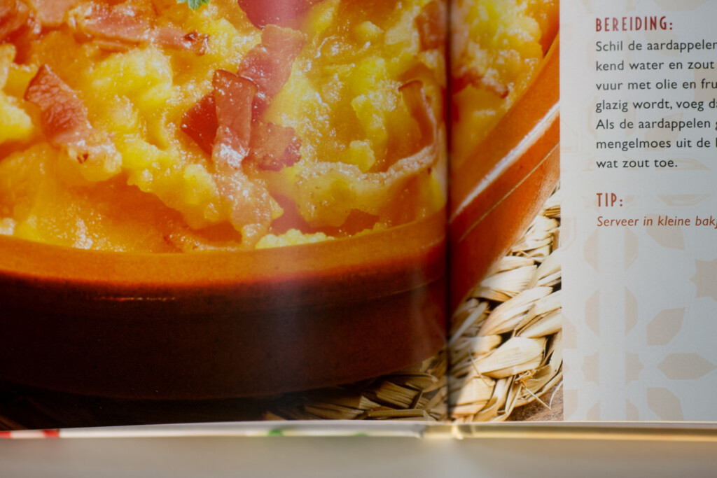 Open cookbook spread showing a recipe with yellow and red dish topped with breadcrumbs, alongside Dutch instruction text and