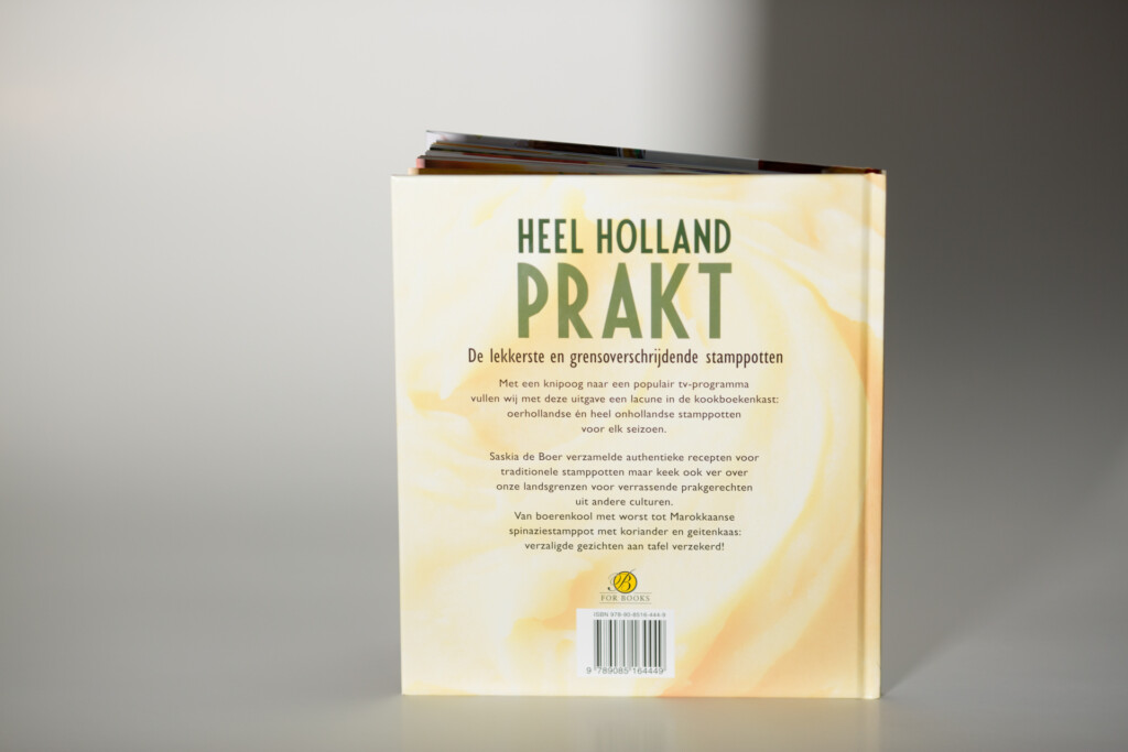 Hardcover book with cream and yellow cover titled Heel Holland Prakt, showing back cover with Dutch text and barcode.