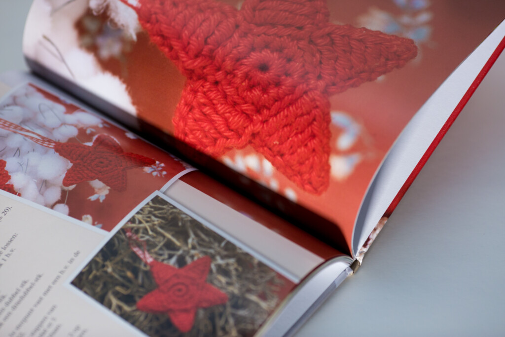 Open hardcover book with red knitted star cover design and embossed detail, showing interior spread with text and image.