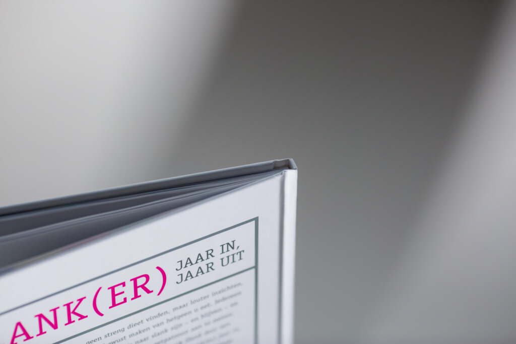 Hardcover book with dark blue spine and white cover featuring magenta text "ANK(ER)" and "JAAR IN JAAR UIT", displayed at an