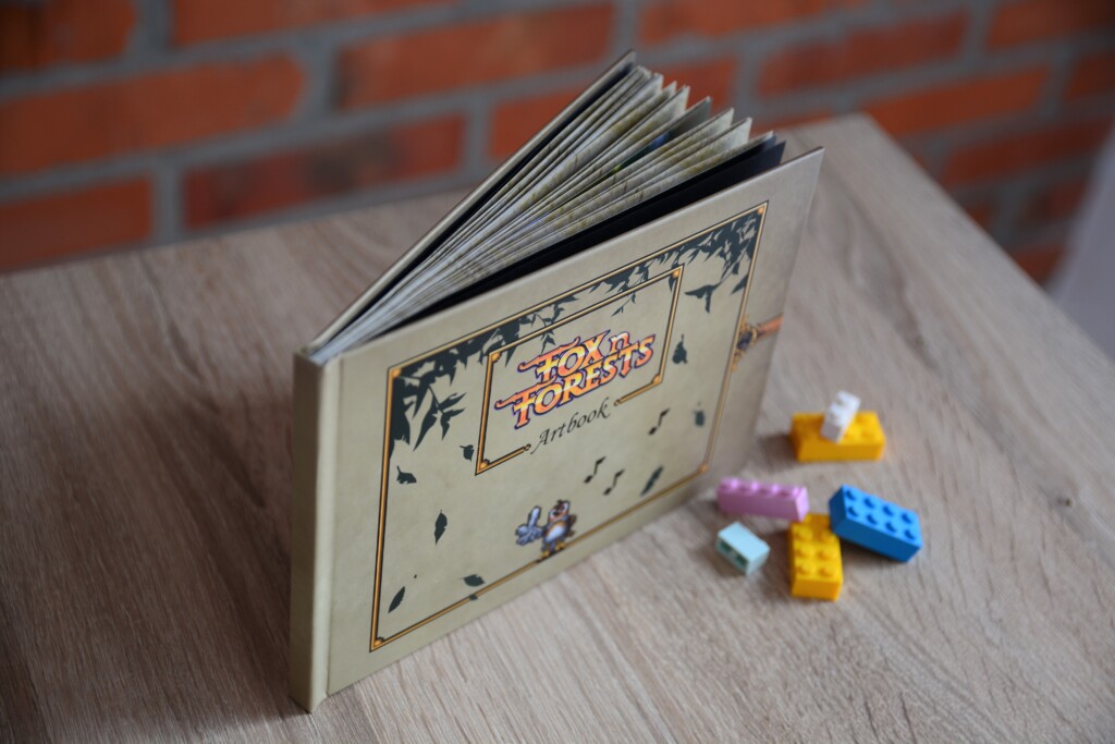 Hardcover book with fanned pages displayed next to coloured plastic game pieces on a wooden surface.