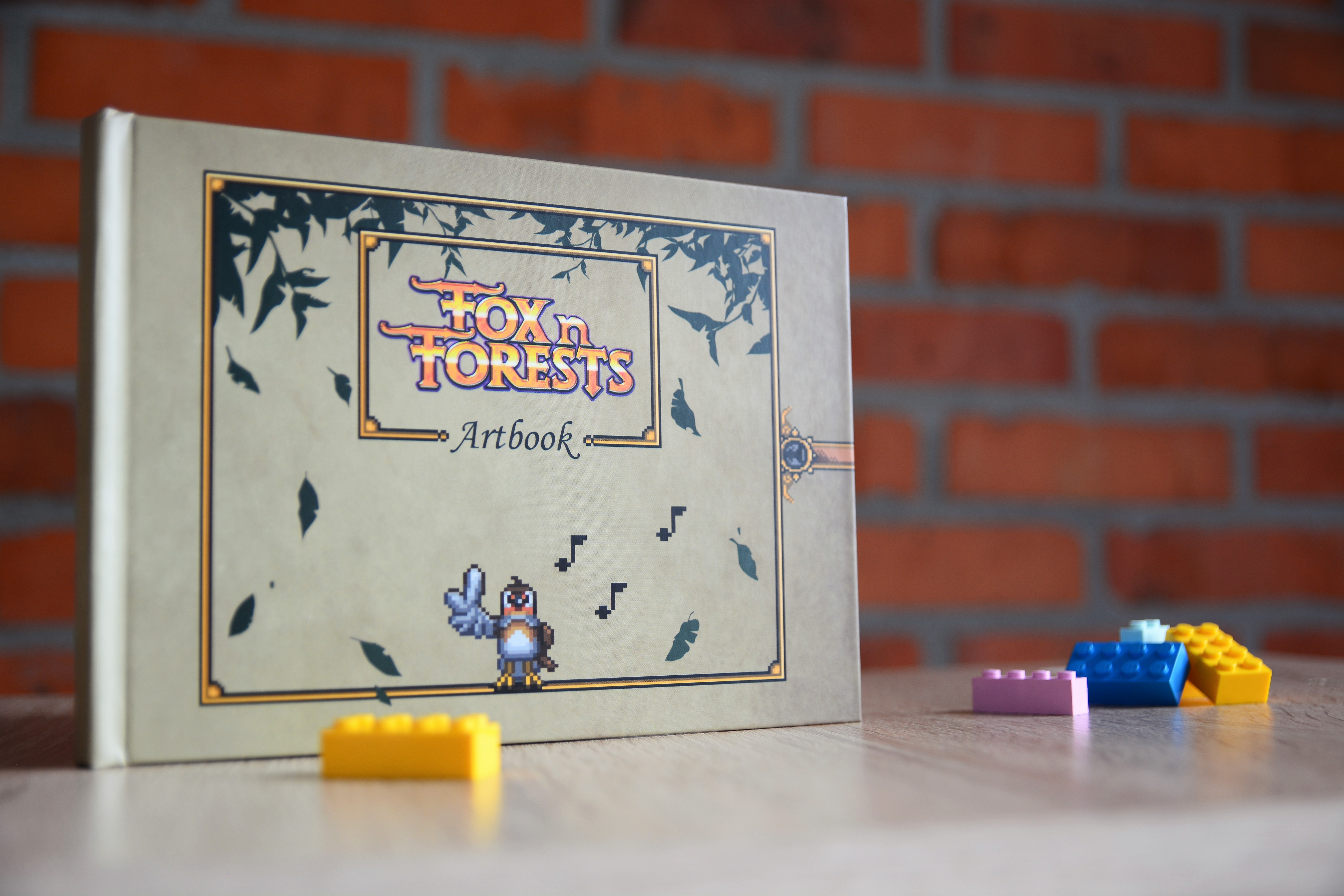 Fox in Forests Artbook hardcover with decorative leaf motifs on cover, displayed next to coloured game pieces against a