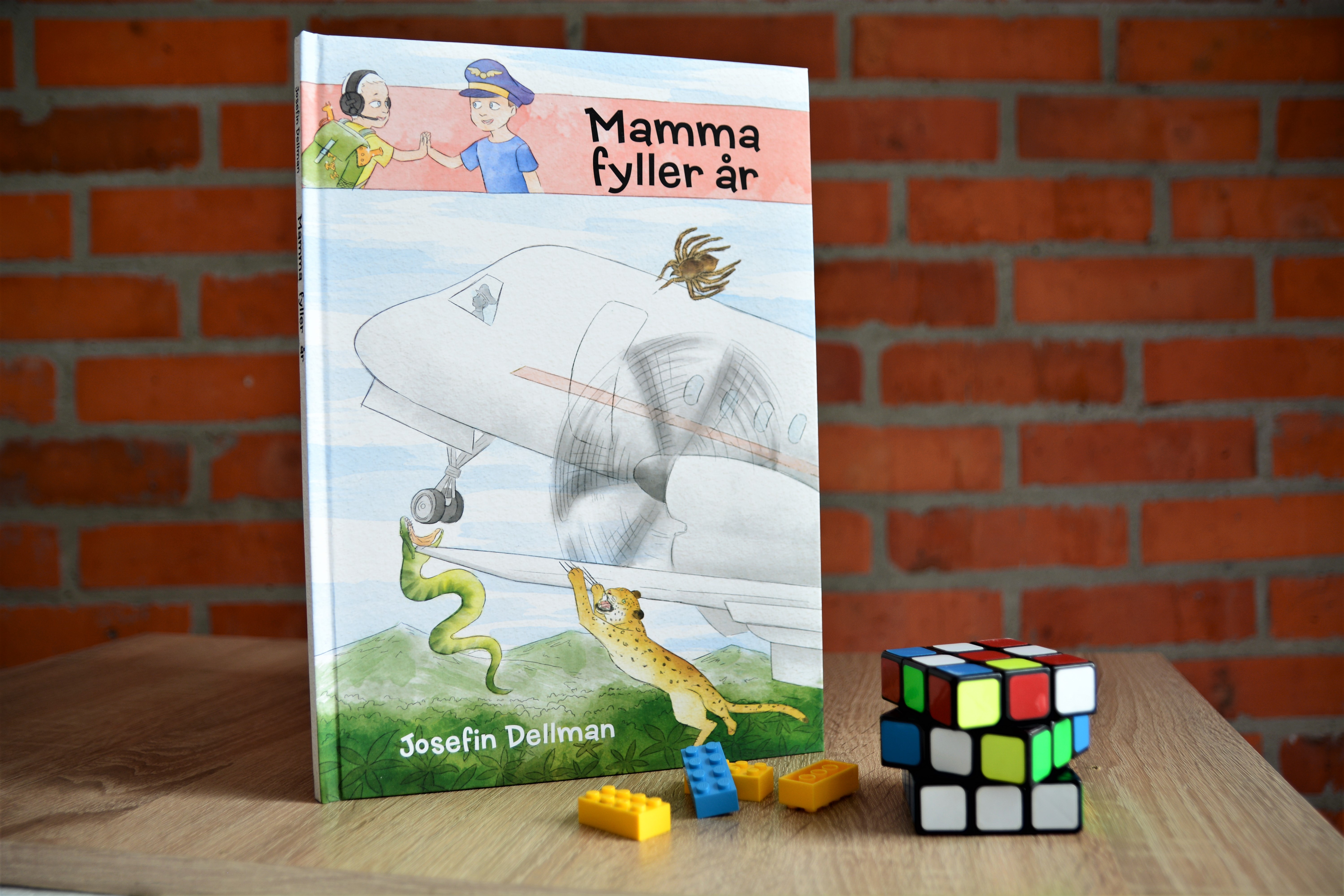 Hardcover children's book titled "Mamma fyller år" by Josefin Dellman, displayed with building blocks and toy animals on