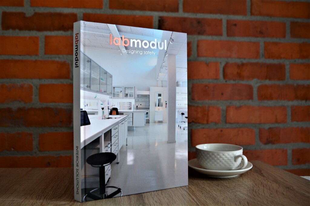 Hardcover catalogue with hot stamping featuring a laboratory interior photograph on the cover, displayed next to a white cup