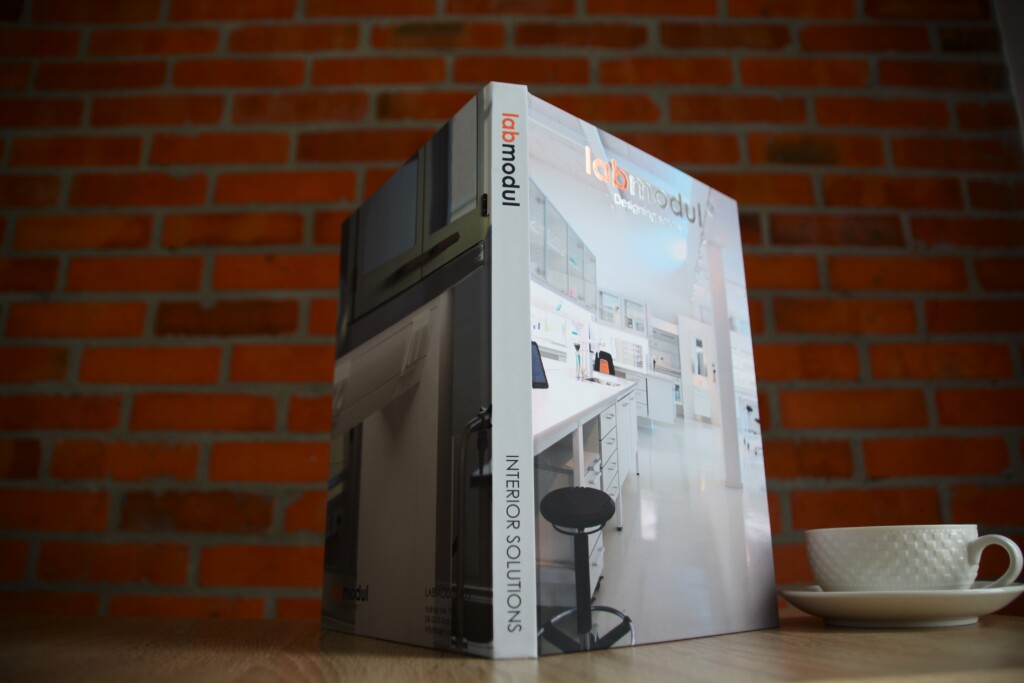 Hardcover catalogue with hot stamping using two different foils, displayed against a red brick wall.
