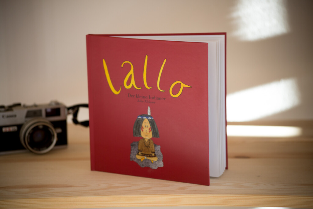 Red hardcover children's book titled "lallo" with an illustrated character on the cover, displayed on a wooden surface with