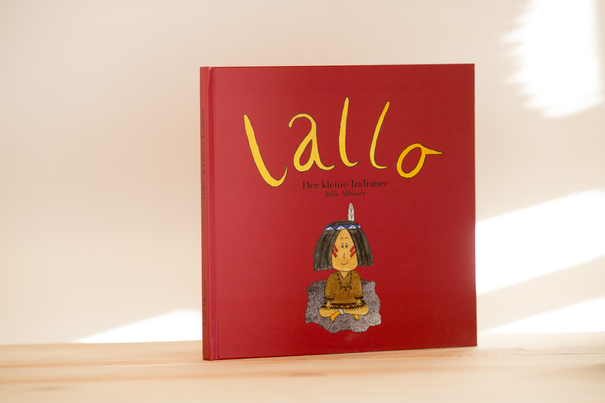 Red hardcover children's book titled "Lallo" with yellow lettering and illustration of a character wearing a blue outfit and