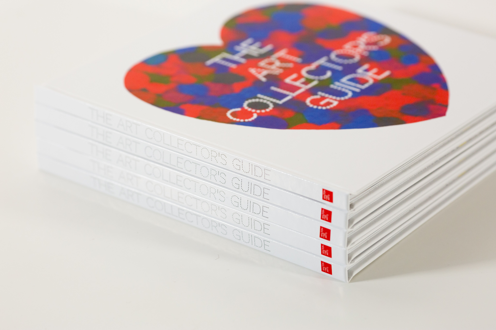 Stack of printed books with colourful heart-shaped cover design and "The Art Collectors Guide" title in white text, showing