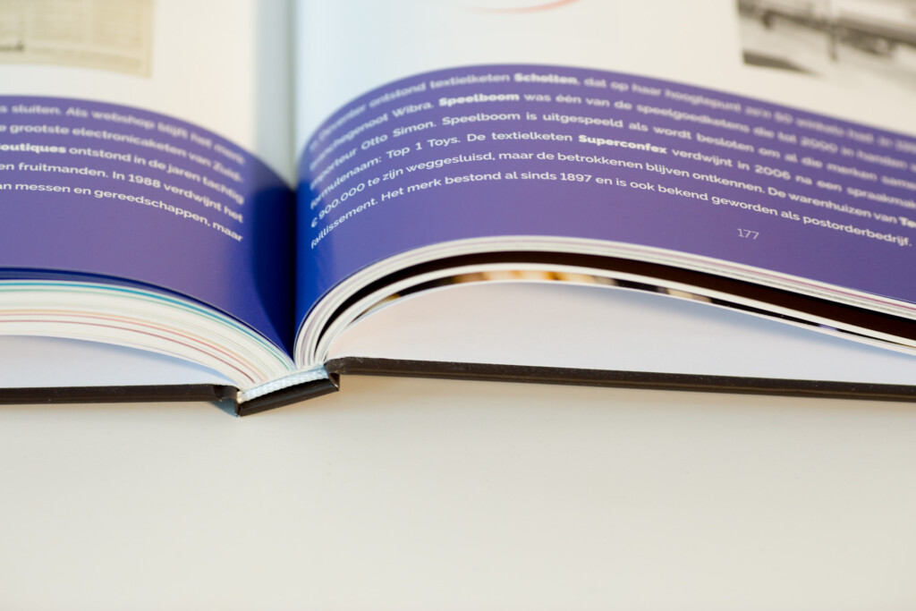 Open hardcover book with purple pages and text in Dutch, showing sewn binding and white paper stock.