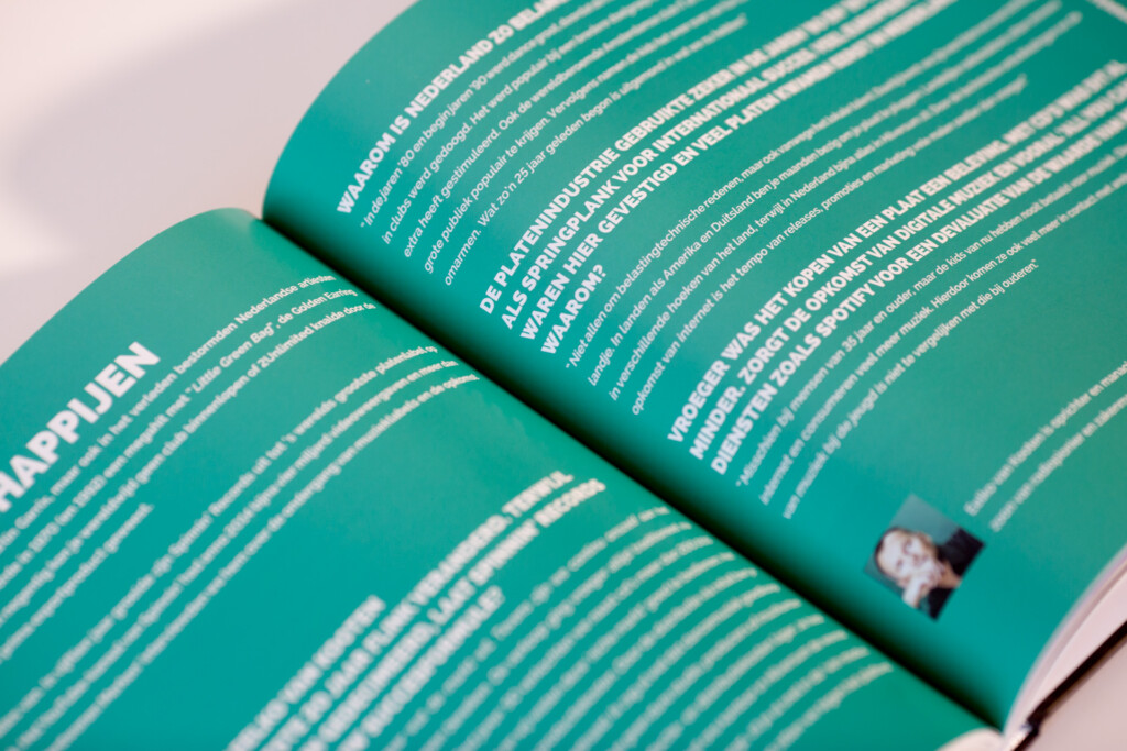 Open turquoise softcover catalogue with white text and horizontal line pattern design on pages.