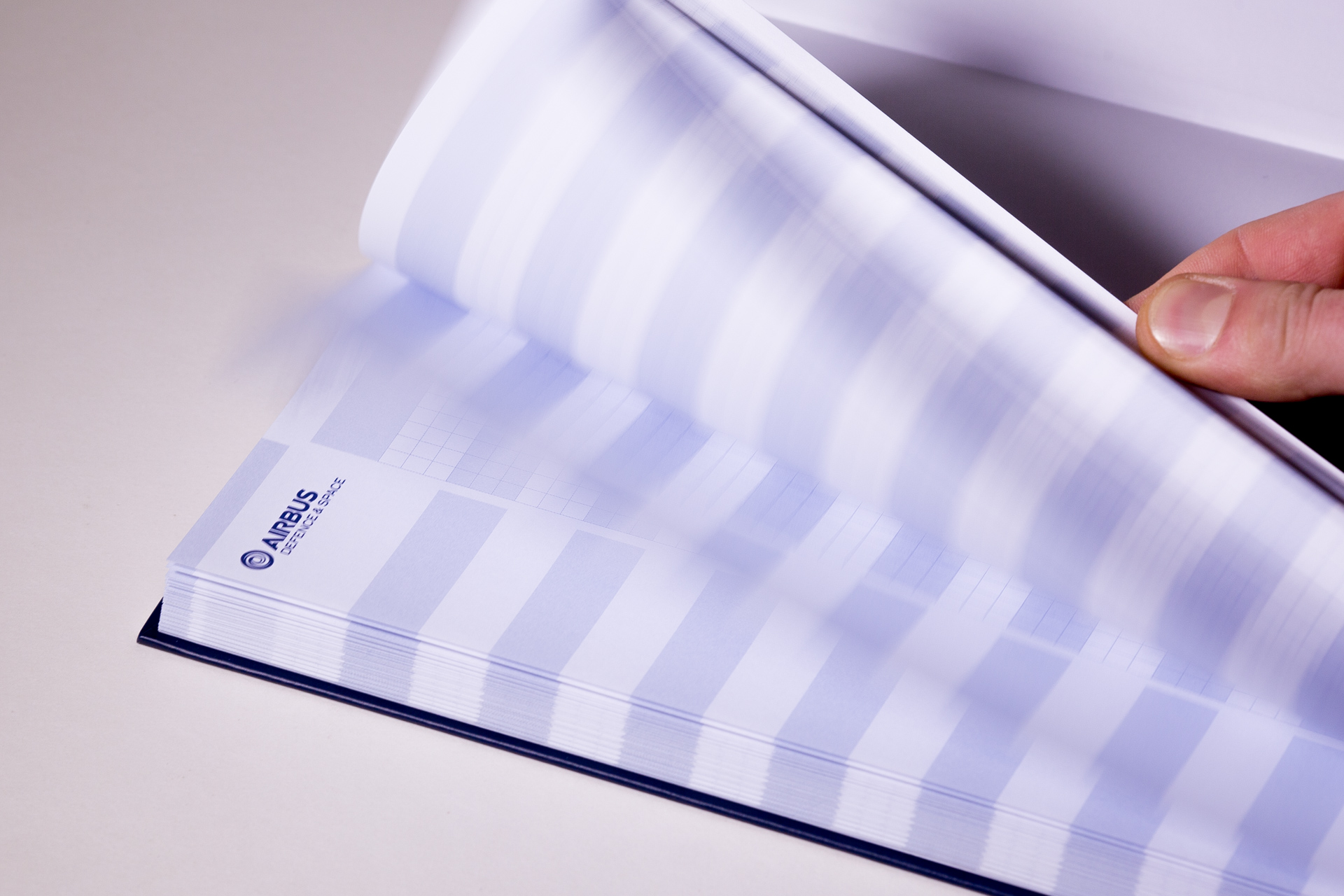 Hand holding open a hardback notebook with lavender and white striped cover and visible logo detail.