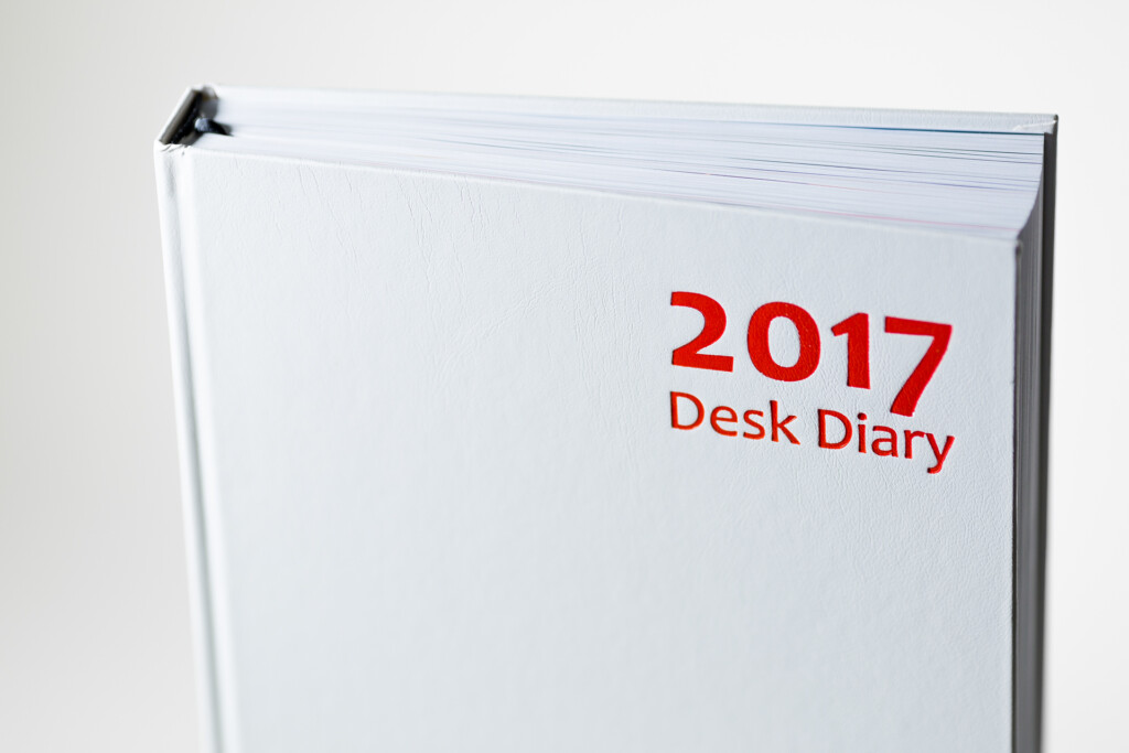 White hardcover desk diary with red "2017 Desk Diary" text on cover and black ribbon bookmark attached.
