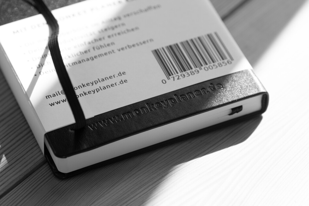 Printed planner with barcode and website details visible on back cover, black binding against grey surface.