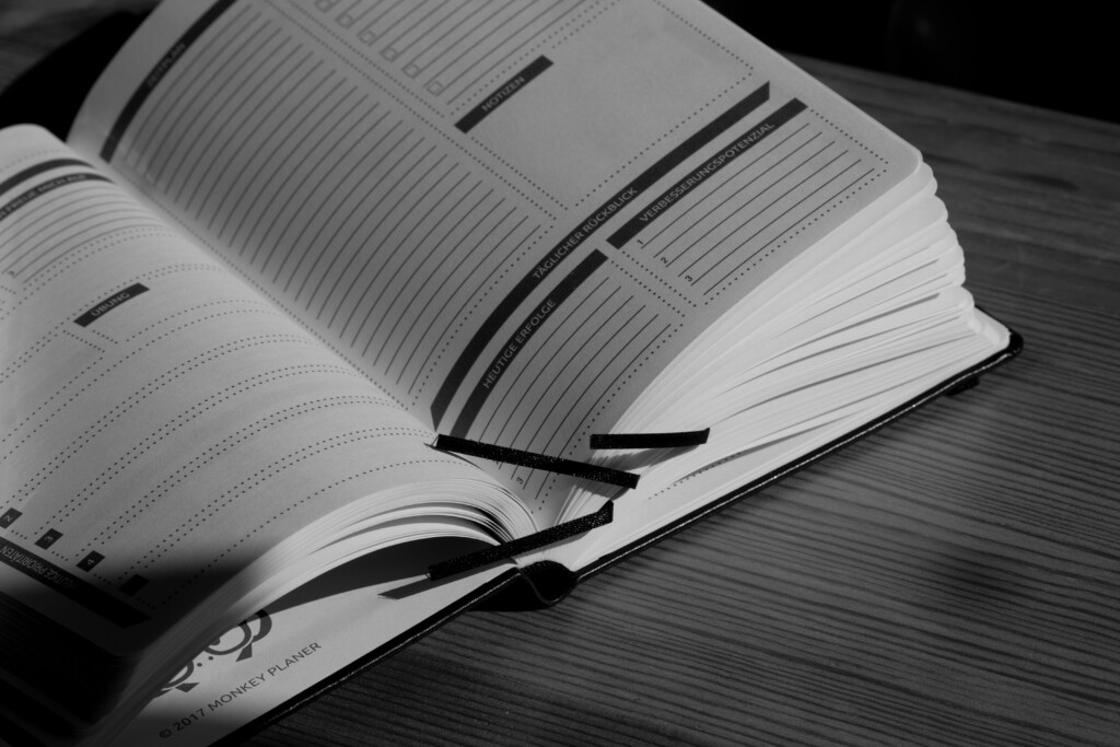 Open planner or notebook with lined pages and black ribbon bookmark, displayed in black and white.