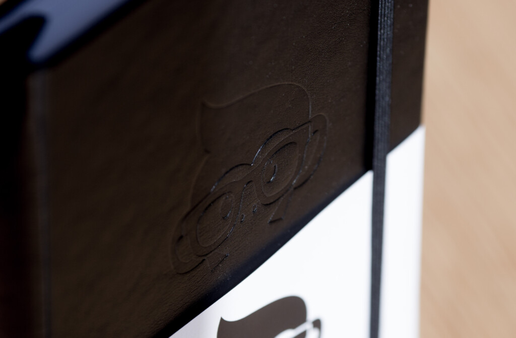 Close-up of embossed logo on dark hardcover book spine with white pages visible.