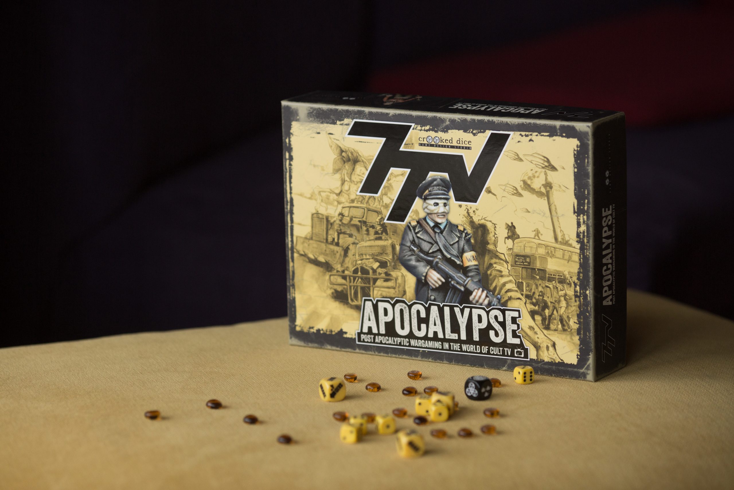 Apocalypse board game box with scattered game pieces and dice on a tan surface.