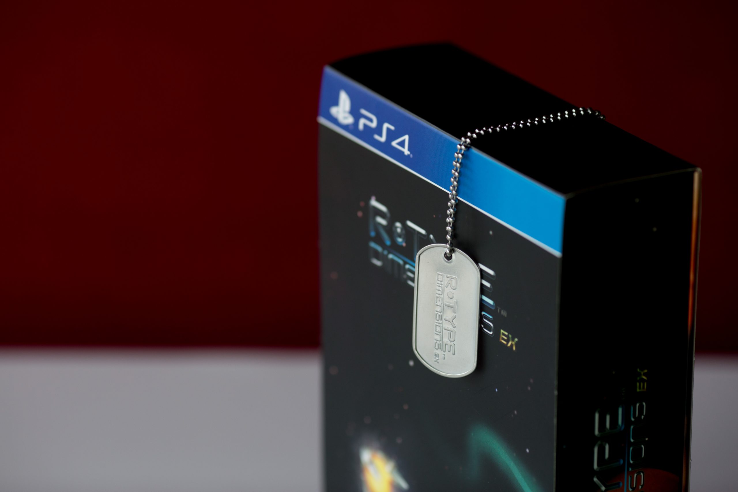 PlayStation 4 game case with metal dog tag hanging from chain attached to blue banner.