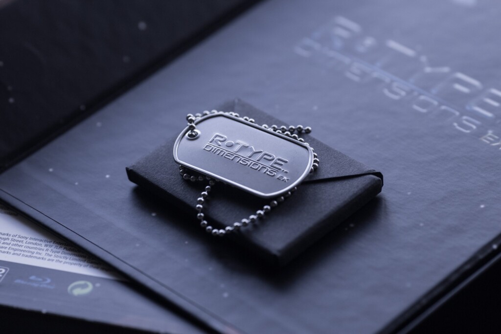 Metal dog tag with chain on black leather pouch, resting on printed materials with blue tinted cover.