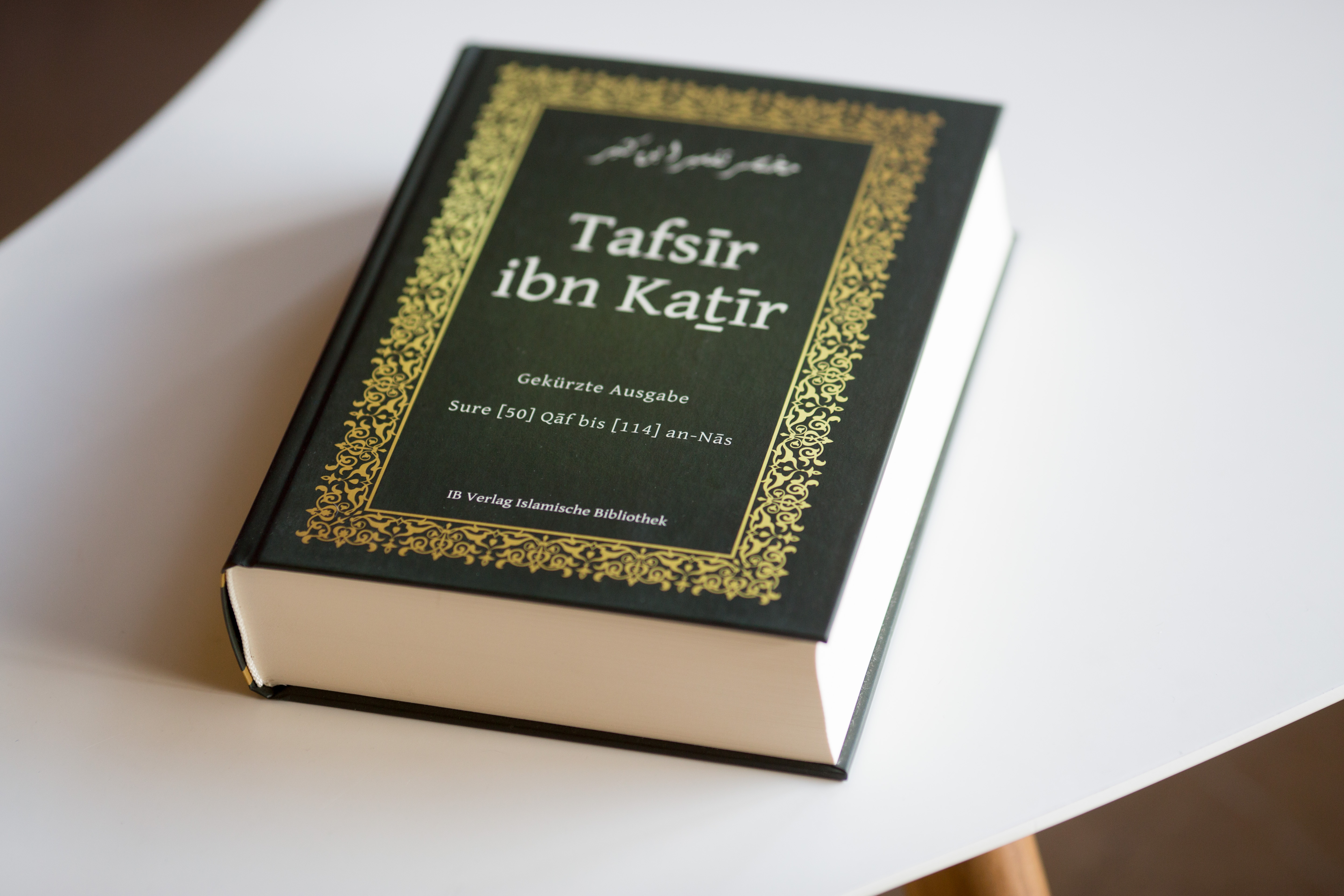 Hardcover book with black cover and gold decorative border, titled Tafsir ibn Katfir, positioned on white surface.