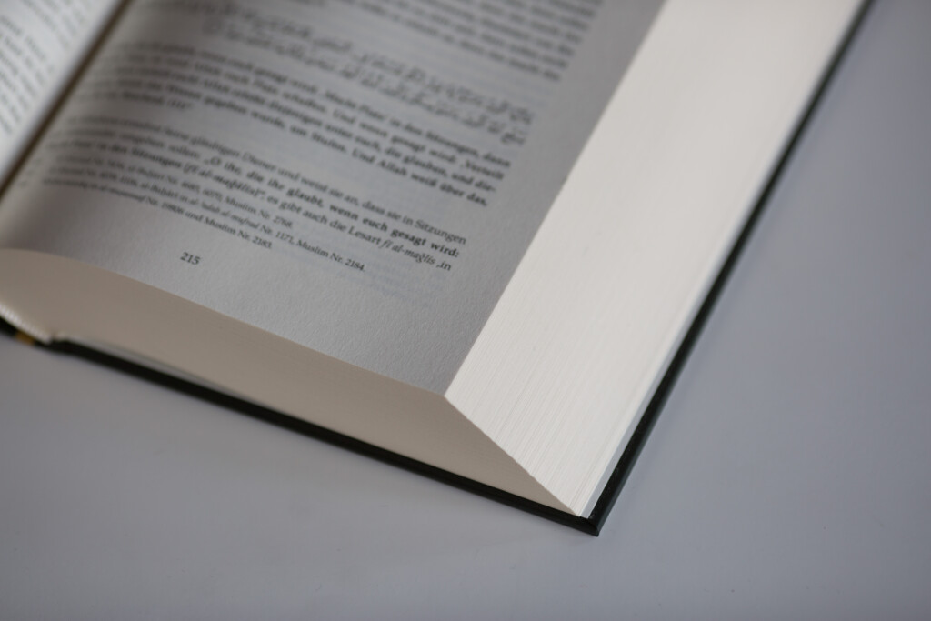 Open hardcover book showing text pages, photographed from above at an angle on grey surface.