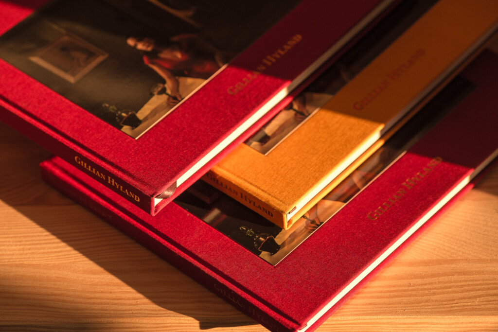 Three hardcover books with gold foil-stamped spines arranged fanned out on a red cloth surface, showing red and orange linen