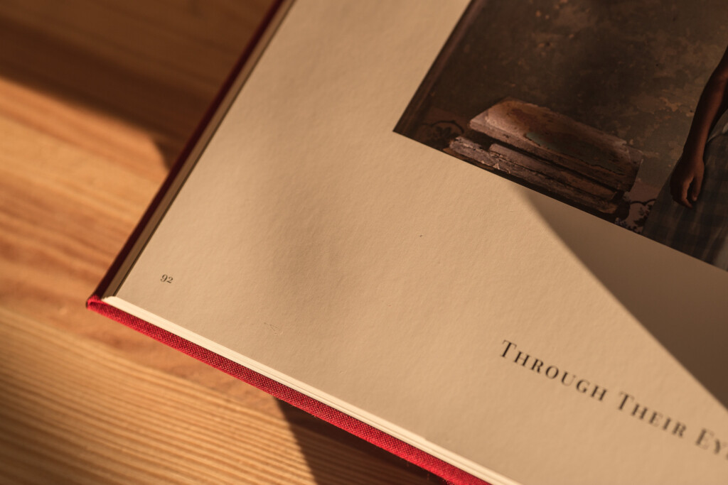 Hardcover book with red cloth spine and gilded page edges, open to show text page reading "Through Their Eyes