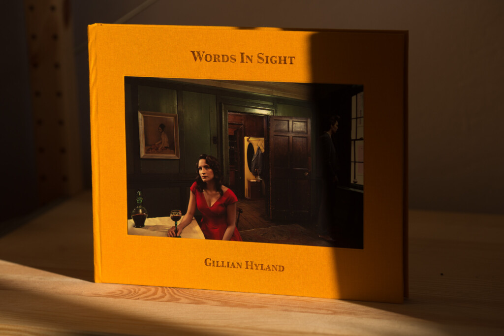 Hardcover book with orange cover titled "Words In Sight" by Gillian Hyland, showing interior photograph of woman in red