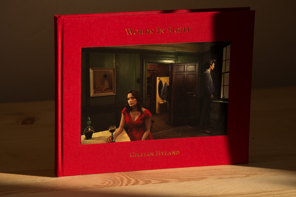 Red hardcover book with gilt lettering on cover, displayed open to show interior photograph of woman in red dress and man in