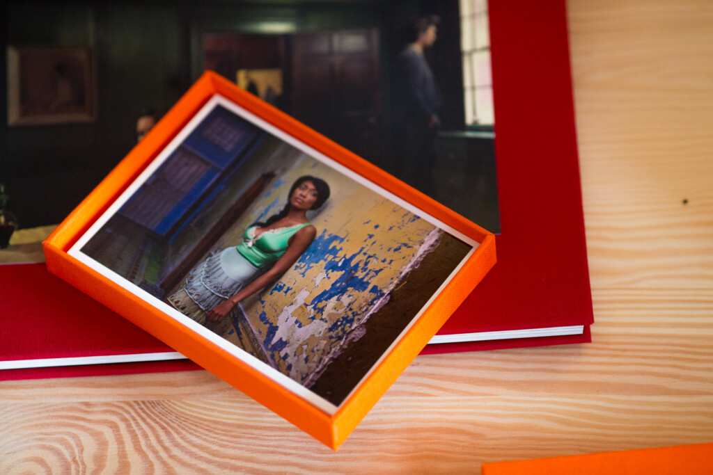 Photo album with orange hardcover case featuring portrait photograph and blue paint-splatter design on wooden surface.