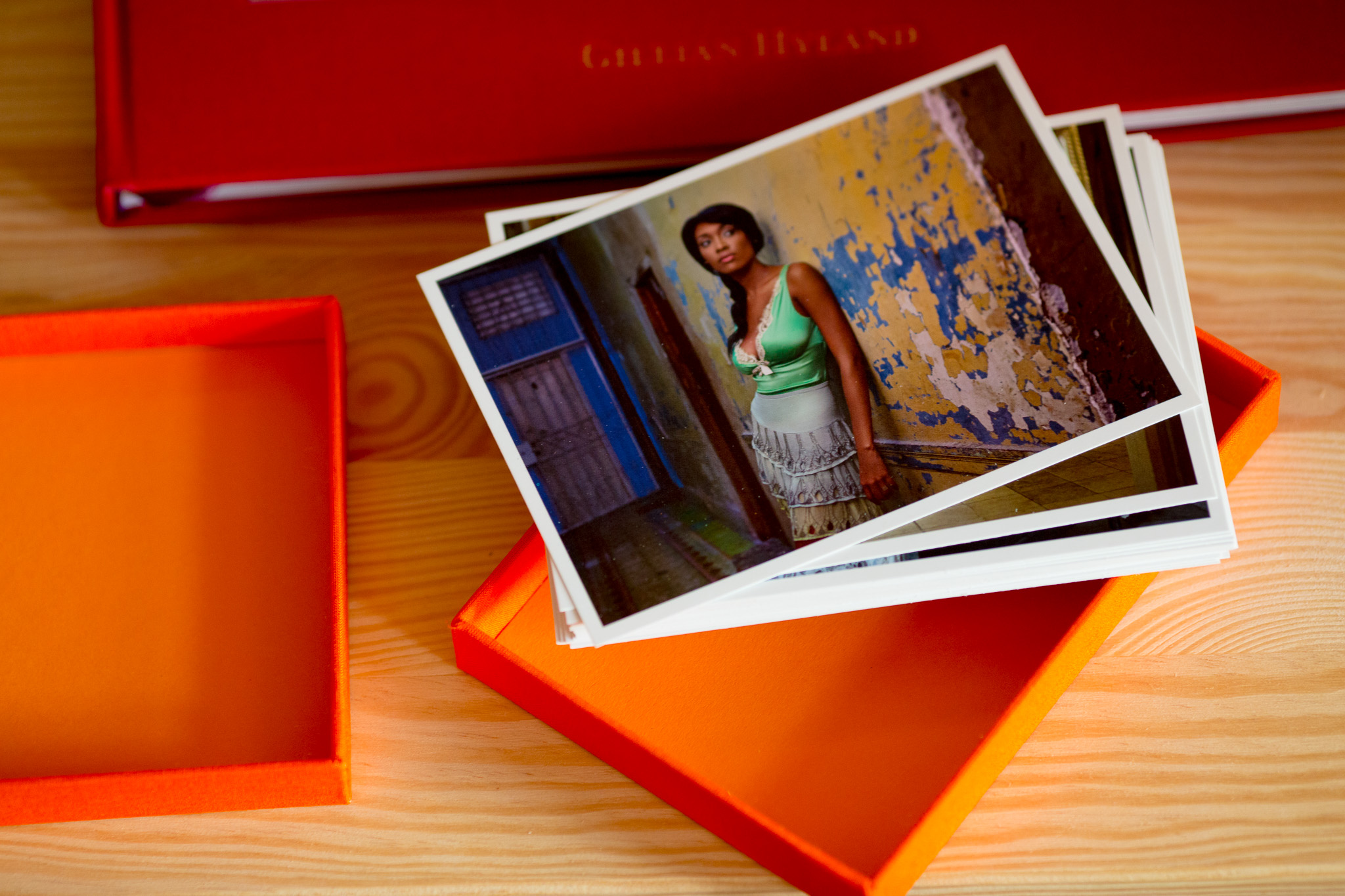 Printed photo album with orange slipcase open, showing interior pages with colour photograph of woman against weathered blue