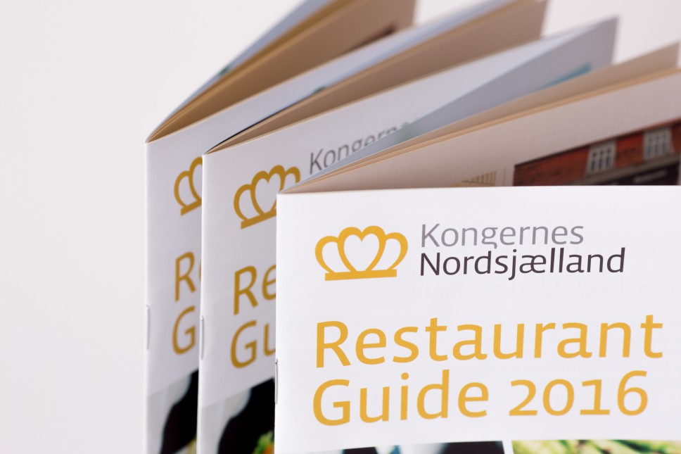 Multiple copies of Kongernes Nordsjælland Restaurant Guide 2016 fanned out, showing gold crown logo and yellow text on white