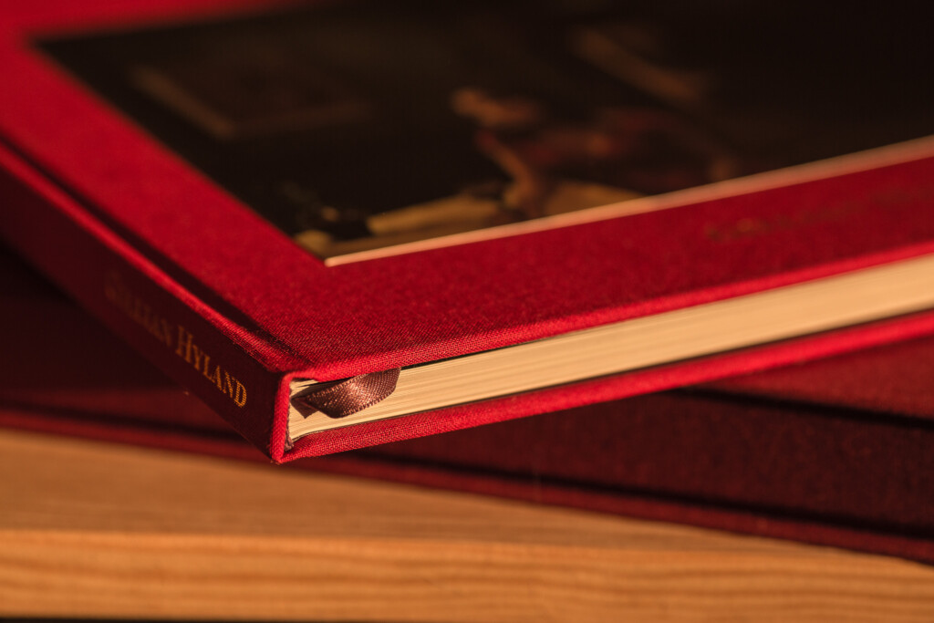 Red hardcover book with gilt-edged pages and gold foil stamping on spine, displayed open on wooden surface.
