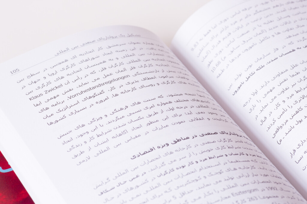 Open book with Arabic text printed on white pages, displayed at an angle against a red surface.