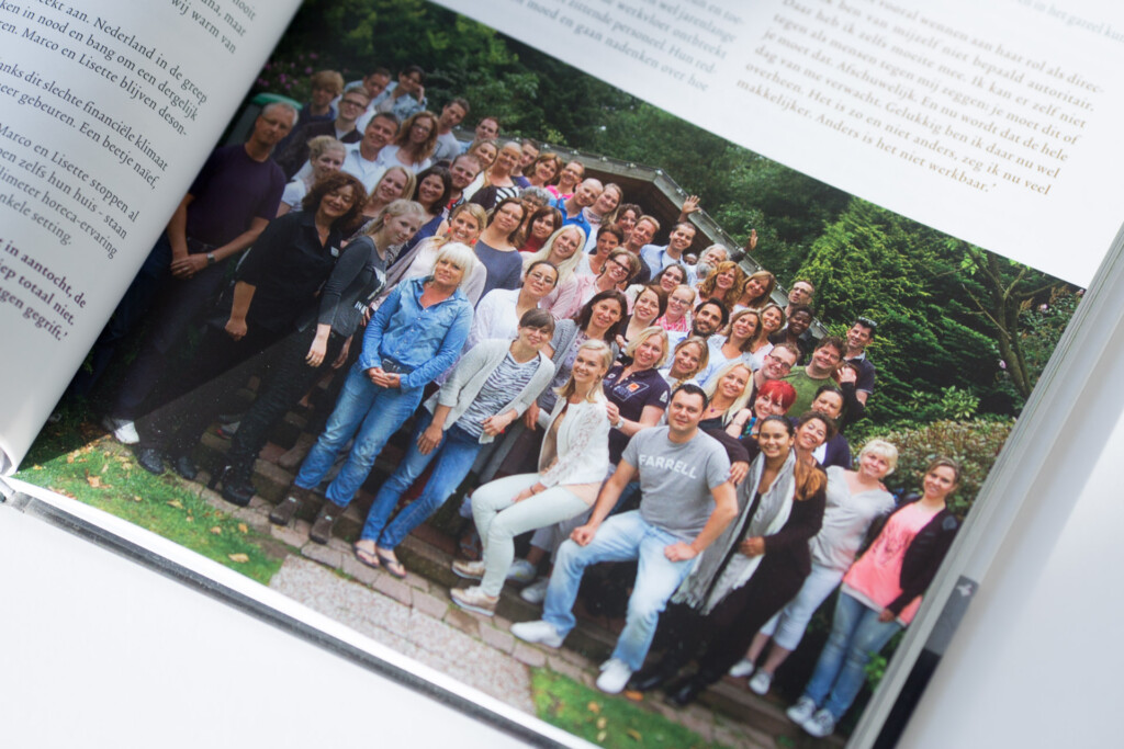 Large group photograph of approximately 50 people standing together outdoors against green foliage, printed on a page within