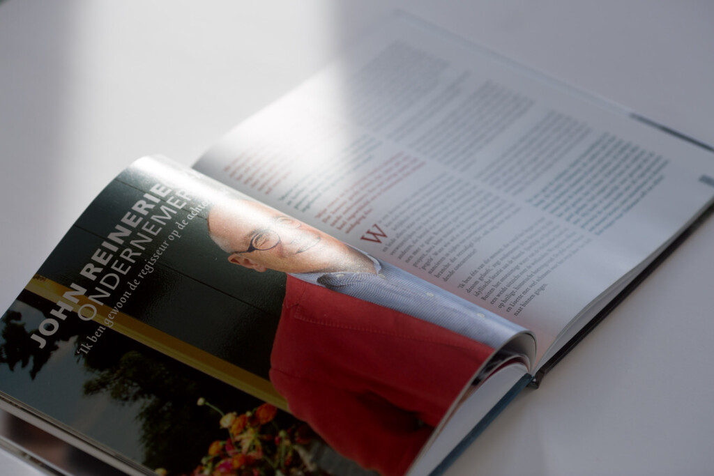 Hardcover book with gloss-laminated cover featuring a woman in a red dress, displayed open alongside a printed catalogue