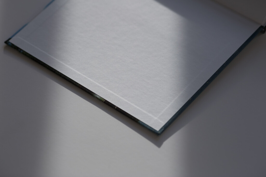 Closed hardcover book with grey cloth cover and black spine, photographed at an angle casting a shadow on a light background.