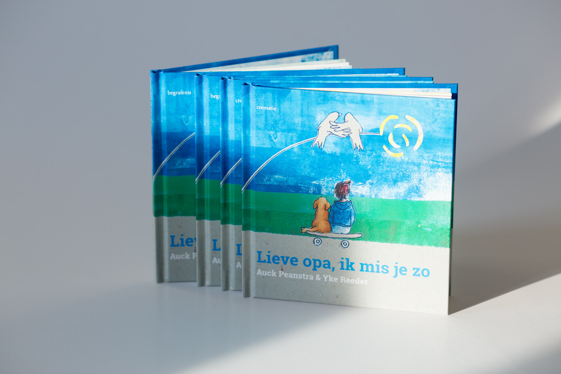 Stack of five copies of children's book "Lieve opa, ik mis je zo" with blue sky and green landscape cover, fanned out to