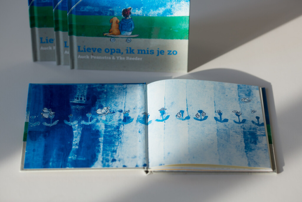 Hardcover book with sewn binding, open to show interior spread featuring blue watercolour illustration with anchors and