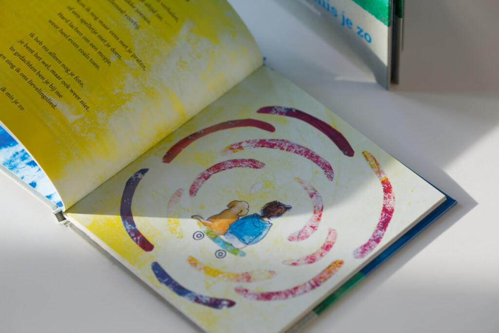 Open children's book with illustration of child surrounded by concentric coloured circles, yellow pages visible at top.